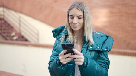Téléchargez les photos : Jeune femme blonde utilisant un smartphone dans la rue - en image libre de droit