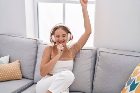 Téléchargez les photos : Jeune femme blonde écoutant de la musique chanter à la maison - en image libre de droit