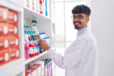 Téléchargez les photos : Jeune homme hispanique pharmacien organiser étagères à la pharmacie - en image libre de droit