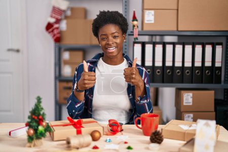 Foto de Mujer afroamericana que trabaja en pequeñas empresas haciendo la decoración de Navidad signo de éxito haciendo gesto positivo con la mano, pulgares arriba sonriendo y feliz. expresión alegre y gesto ganador. - Imagen libre de derechos