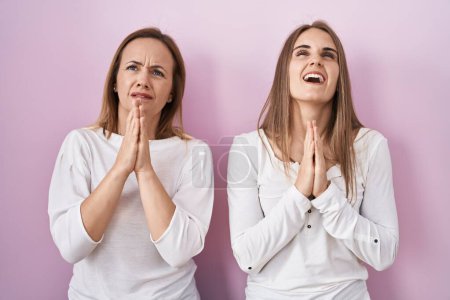 Photo for Middle age mother and young daughter standing over pink background begging and praying with hands together with hope expression on face very emotional and worried. begging. - Royalty Free Image