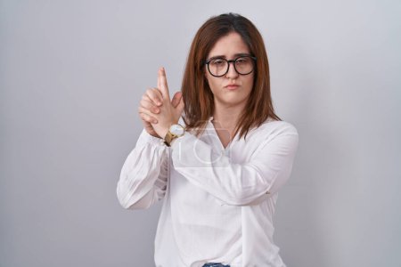 Photo for Brunette woman standing over white isolated background holding symbolic gun with hand gesture, playing killing shooting weapons, angry face - Royalty Free Image