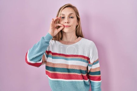 Téléchargez les photos : Young blonde woman standing over pink background mouth and lips shut as zip with fingers. secret and silent, taboo talking - en image libre de droit