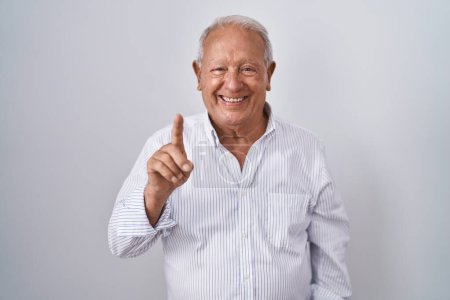 Téléchargez les photos : Senior man with grey hair standing over isolated background showing and pointing up with finger number one while smiling confident and happy. - en image libre de droit