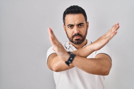 Téléchargez les photos : Jeune homme hispanique avec barbe portant des vêtements décontractés sur fond blanc expression de rejet croisant les bras faisant signe négatif, visage en colère - en image libre de droit
