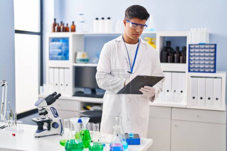 Photo for Young hispanic man scientist writing report working at laboratory - Royalty Free Image