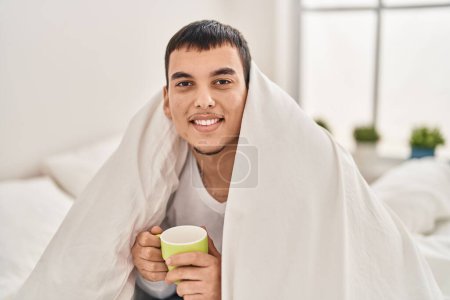 Téléchargez les photos : Jeune homme buvant une tasse de café assis sur le lit dans la chambre - en image libre de droit