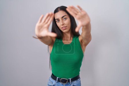 Foto de Young woman standing over isolated background doing frame using hands palms and fingers, camera perspective - Imagen libre de derechos