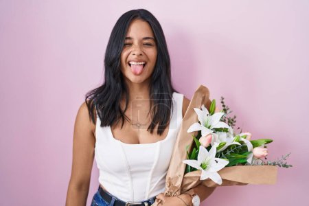 Téléchargez les photos : Brunette femme tenant bouquet de fleurs blanches langue collante heureux avec une expression drôle. concept d'émotion. - en image libre de droit