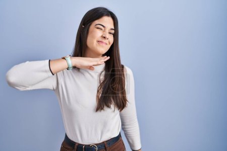 Photo for Young brunette woman standing over blue background cutting throat with hand as knife, threaten aggression with furious violence - Royalty Free Image