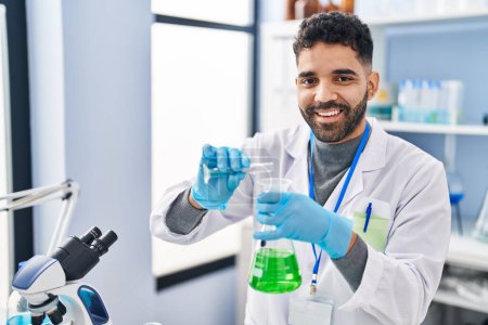 Téléchargez les photos : Jeune homme hispanique portant l'uniforme scientifique mesurant le liquide au laboratoire - en image libre de droit