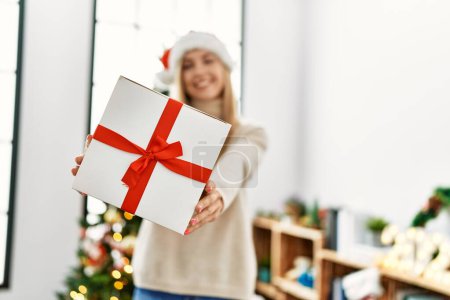 Téléchargez les photos : Jeune femme blonde tenant cadeau debout près de l'arbre de Noël à la maison - en image libre de droit