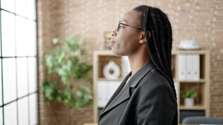 Téléchargez les photos : Femme afro-américaine ouvrière debout avec une expression détendue au bureau - en image libre de droit