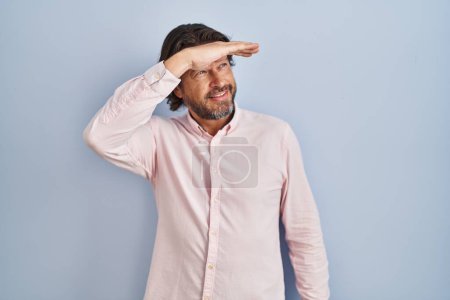 Photo for Handsome middle age man wearing elegant shirt background very happy and smiling looking far away with hand over head. searching concept. - Royalty Free Image