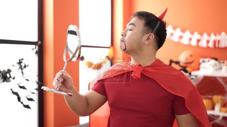 Téléchargez les photos : Jeune homme chinois portant costume diable regardant miroir à la maison - en image libre de droit