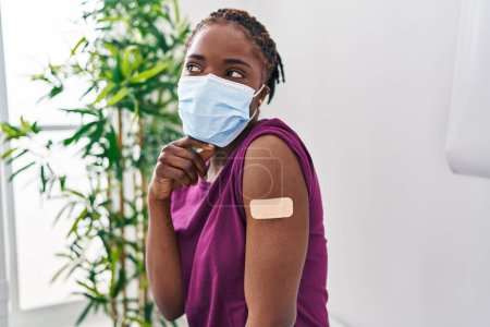 Photo for Beautiful black woman getting vaccine showing arm with band aid serious face thinking about question with hand on chin, thoughtful about confusing idea - Royalty Free Image