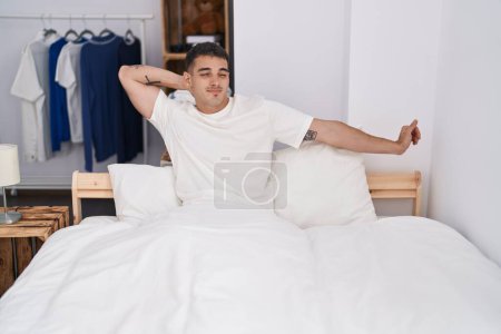 Photo for Young hispanic man waking up stretching arms at bedroom - Royalty Free Image