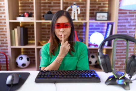Téléchargez les photos : Femme chinoise du Moyen Âge portant des lunettes de réalité virtuelle demandant à être calme avec le doigt sur les lèvres. silence et concept secret. - en image libre de droit