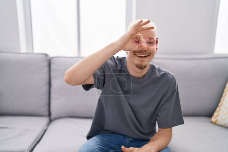 Foto de Joven hombre caucásico con gafas de realidad virtual sonriendo feliz haciendo signo de ok con la mano en el ojo mirando a través de los dedos - Imagen libre de derechos