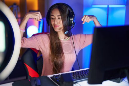 Photo for Young hispanic woman playing video games showing arms muscles smiling proud. fitness concept. - Royalty Free Image