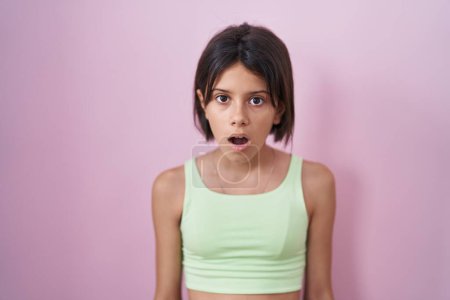 Foto de Chica joven de pie sobre fondo rosa en la cara de choque, mirando escéptico y sarcástico, sorprendido con la boca abierta - Imagen libre de derechos