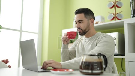 Foto de Joven hispano usando laptop bebiendo café en casa - Imagen libre de derechos