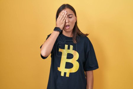 Téléchargez les photos : Jeune femme hispanique portant Bitcoin t-shirt bâillement fatigué couvrant demi-visage, oeil et bouche avec la main. mal au visage dans la douleur. - en image libre de droit