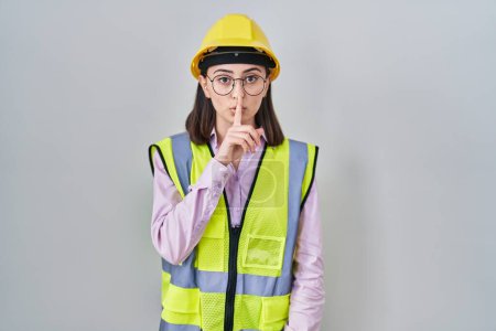 Photo for Hispanic girl wearing builder uniform and hardhat asking to be quiet with finger on lips. silence and secret concept. - Royalty Free Image