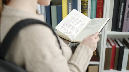 Photo for Young blonde woman student reading book at library university - Royalty Free Image