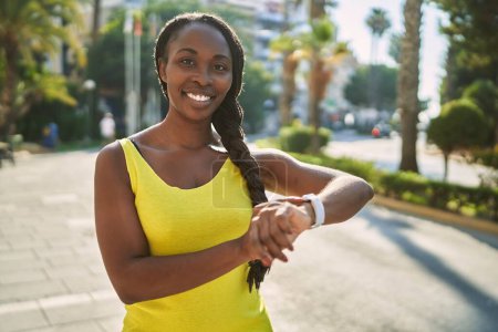 Photo for African american woman wearing sportswear looking stopwatch at street - Royalty Free Image