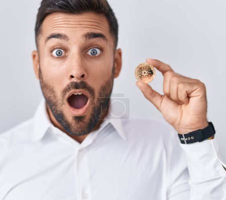 Photo for Handsome hispanic man holding cardano cryptocurrency coin scared and amazed with open mouth for surprise, disbelief face - Royalty Free Image
