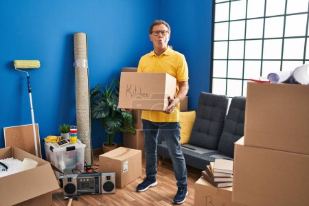 Photo for Senior man moving to a new home holding cardboard box making fish face with mouth and squinting eyes, crazy and comical. - Royalty Free Image