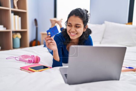 Photo for Young latin woman using laptop and credit card lying on bed at bedroom - Royalty Free Image