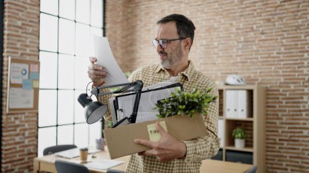 Photo for Middle age man business worker dismissed holding cardboard box reading paperwork at office - Royalty Free Image