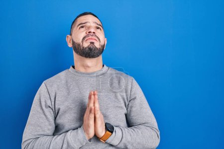Photo for Hispanic man standing over blue background begging and praying with hands together with hope expression on face very emotional and worried. begging. - Royalty Free Image