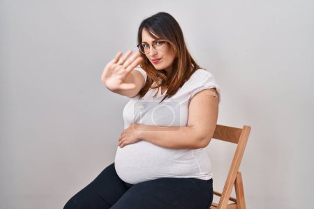 Photo for Pregnant woman wearing band aid for vaccine injection with open hand doing stop sign with serious and confident expression, defense gesture - Royalty Free Image