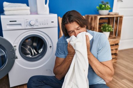 Photo for Middle age man washing clothes smelling towel at laundry room - Royalty Free Image
