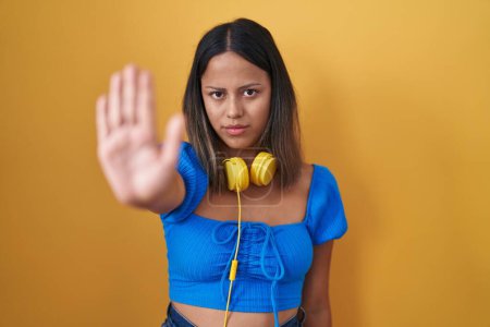 Photo for Hispanic young woman standing over yellow background doing stop sing with palm of the hand. warning expression with negative and serious gesture on the face. - Royalty Free Image