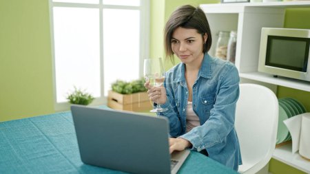 Téléchargez les photos : Jeune femme caucasienne utilisant un ordinateur portable boire du vin à la maison - en image libre de droit