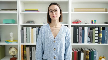 Téléchargez les photos : Jeune belle étudiante hispanique debout avec une expression détendue à l'université de la bibliothèque - en image libre de droit