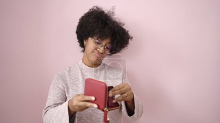 Foto de Joven mujer afroamericana mostrando cartera vacía sobre fondo rosa aislado - Imagen libre de derechos