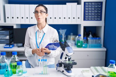 Photo for Young brunette woman working at scientist laboratory making fish face with lips, crazy and comical gesture. funny expression. - Royalty Free Image