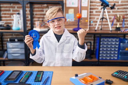 Photo for Little caucasian boy at school scientist laboratory winning first prize pointing thumb up to the side smiling happy with open mouth - Royalty Free Image