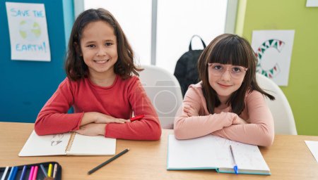 Téléchargez les photos : Adorables filles étudiants assis sur la table souriant confiant à la salle de classe - en image libre de droit