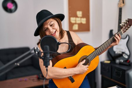 Foto de Mujer de mediana edad músico cantando canción tocando guitarra clásica en el estudio de música - Imagen libre de derechos