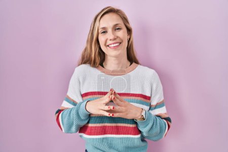 Téléchargez les photos : Young blonde woman standing over pink background hands together and fingers crossed smiling relaxed and cheerful. success and optimistic - en image libre de droit