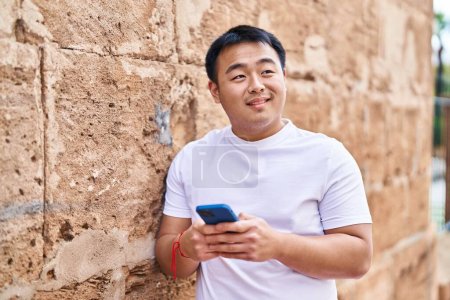 Photo for Young chinese man smiling confident using smartphone at street - Royalty Free Image