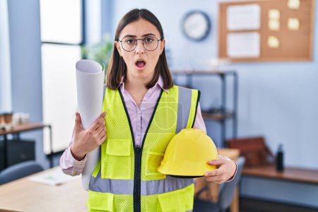 Photo for Hispanic girl architect holding build project blueprints in shock face, looking skeptical and sarcastic, surprised with open mouth - Royalty Free Image