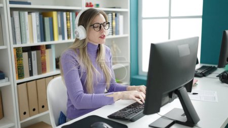 Téléchargez les photos : Young blonde woman student using computer and headphones studying at library university - en image libre de droit