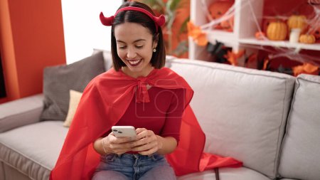 Téléchargez les photos : Young beautiful hispanic woman wearing devil costume using smartphone at home - en image libre de droit